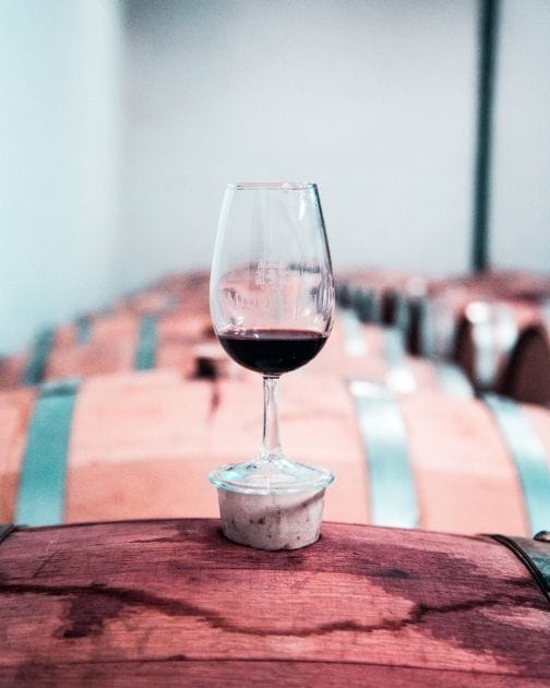 Red wine tasting glass on top of a barrel surrounded by wine barrels 