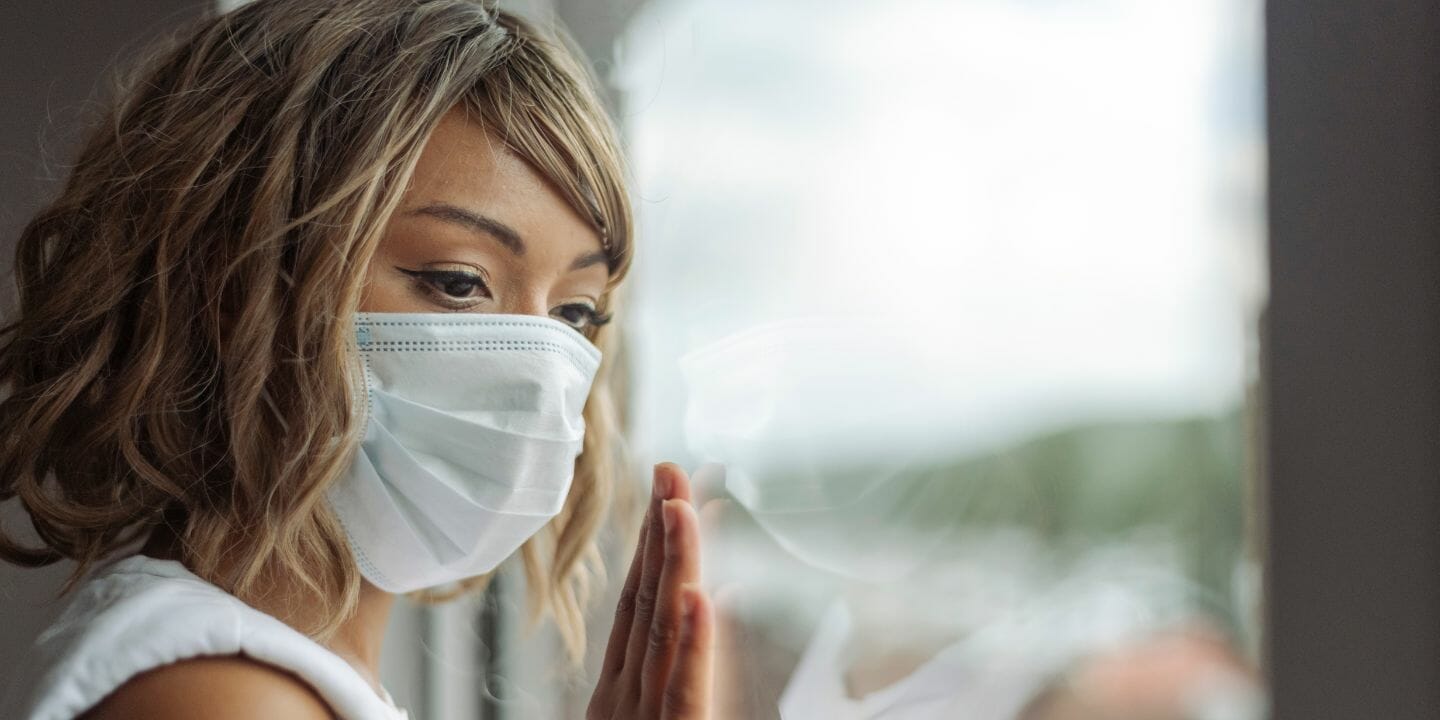 a woman wearing a surgical mask looks out the window during Covid 19