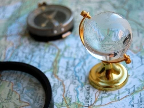 Globe paperweight on top of a map with a compass and part of a magnifying lens in the background