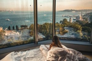 lady in bed looking out to a panoramic view of the sea