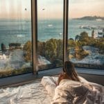 lady in bed looking out to a panoramic view of the sea
