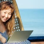 Lady with a stump right hand smiling at the camera in an egg hammock while working on her laptop