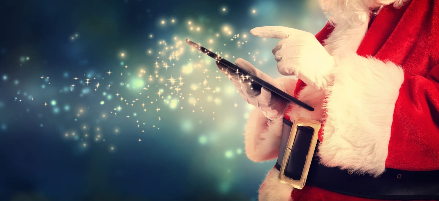 Santa Claus using a tablet, with sparkles emanating from it against a blue, festive background.