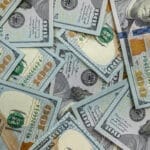 A scattered pile of U.S. one hundred dollar bills covering the background