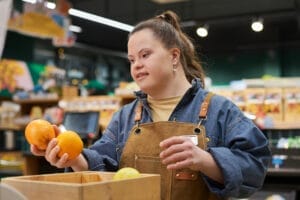 A woman with Down syndrome holding two oranges in her hands while checking a box of fruits.