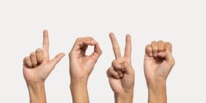 Four hands spelling "LOVE" in American Sign Language against a light background highlight the essence of communication, while automated accessibility testing ensures this message is universally understood.