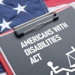 A clipboard reading “Americans with Disabilities Act” with wheelchair and scale icons on a US flag, symbolizing ADA Website Lawsuits.
