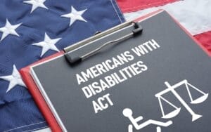 A clipboard reading “Americans with Disabilities Act” with wheelchair and scale icons on a US flag, symbolizing ADA Website Lawsuits.