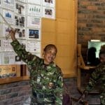 Two women from the The Black Mambas anti-poaching unit stand in front of graphs and charts showing their mission, their tactics, their challenges and their success rate.